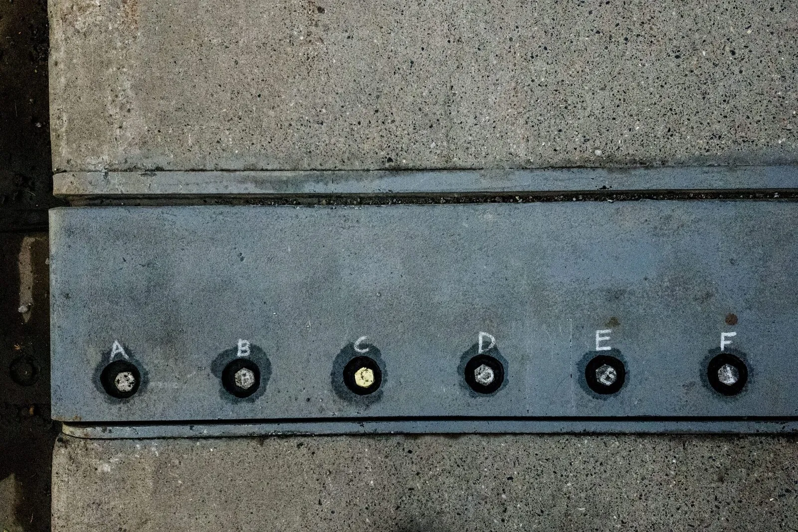 Concrete and metal bolts with alphabet letters on sidewalk in Banff, Canada.
