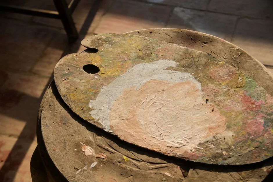 A sunlit rustic wooden painter's palette with mixed colors laid on a wooden surface.