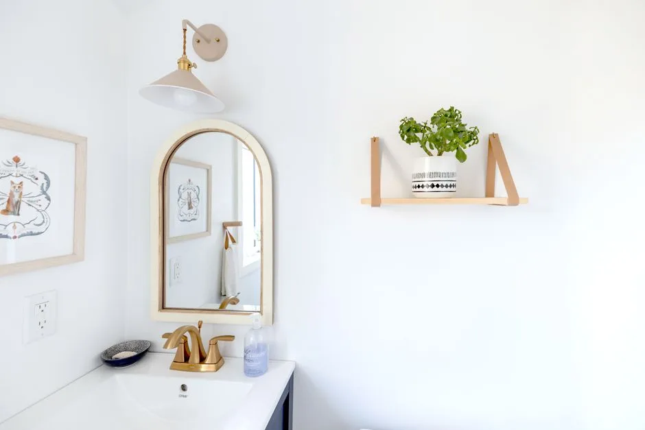 Bright and simple bathroom interior with a gold-framed mirror and decorative shelf.