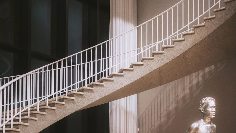 Elegant concrete staircase with white railing and silver sculpture indoors, exuding modern style.