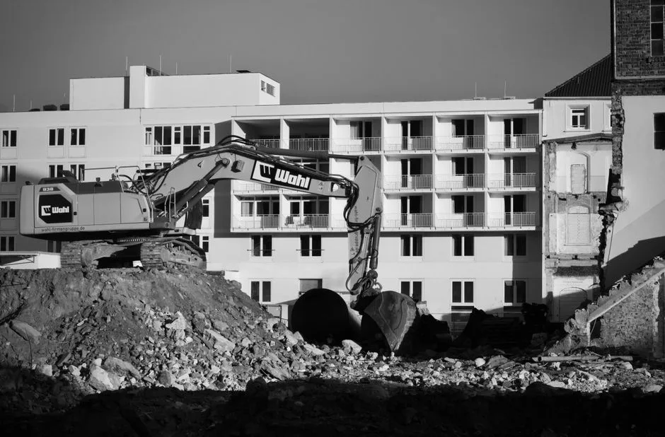 Black and white image of an urban construction site with an excavator in front of a building.