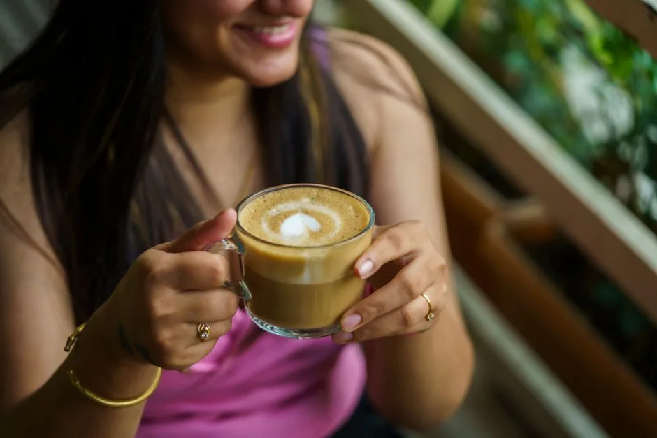 A woman holding a frothy cappuccino in a relaxing setting, sipping coffee.
