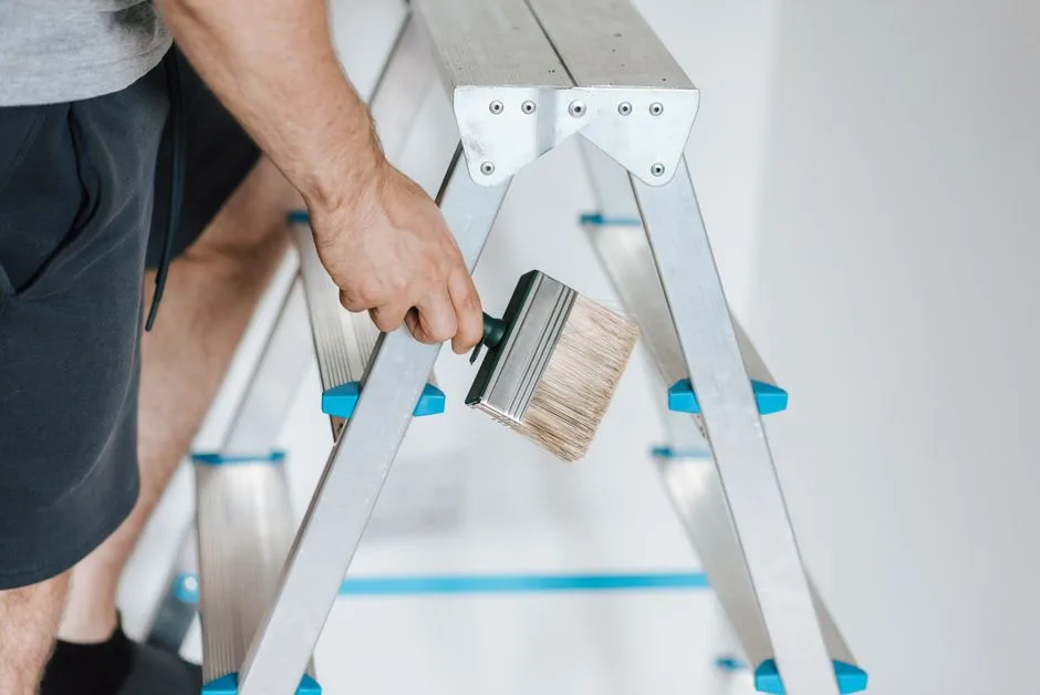 Side view of crop anonymous male master standing on ladder with tool while painting walls in flat