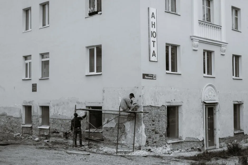 Black and white of anonymous male workers repairing aged shabby wall of residential building
