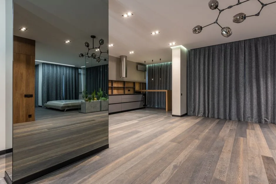 Spacious room in apartment with wooden floor decorated with mirrored pillar and green plants