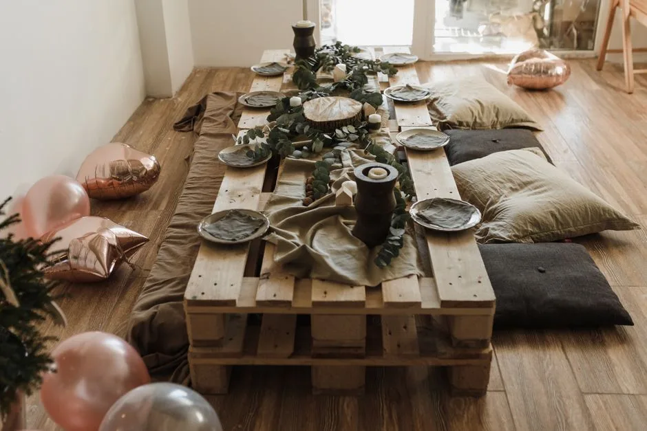 A cozy indoor party setup featuring a wooden pallet table, decorations, and casual seating.