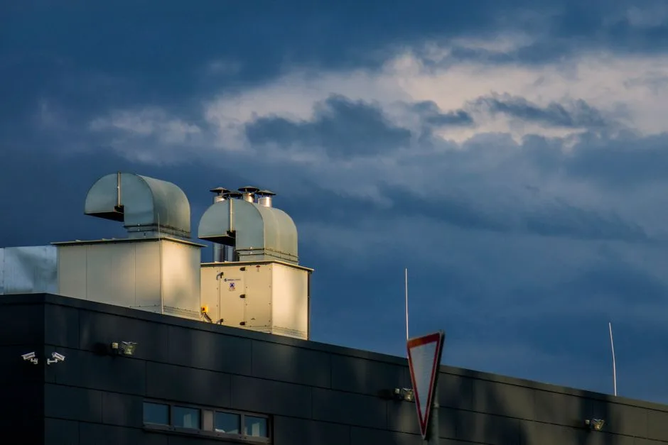 Low angle of metal pipes of ventilation system located on rooftop of industrial building against cloudy sky