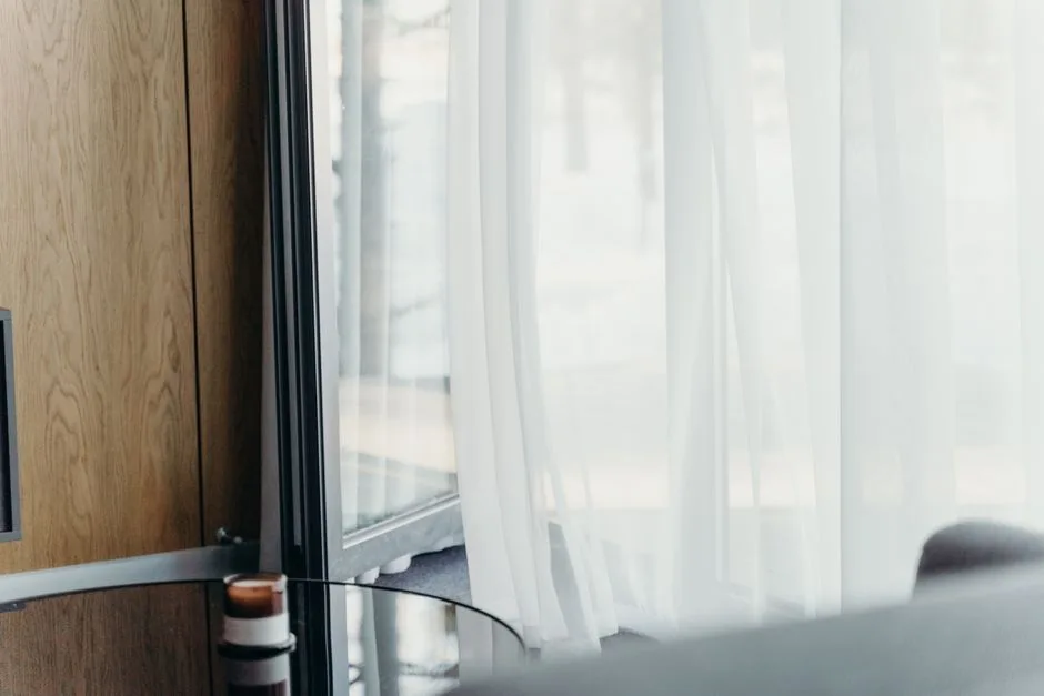 A modern hotel room with sheer curtains softly lit, emphasizing luxury and tranquility.