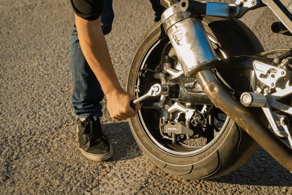 A close-up of a person using a wrench to repair a motorcycle wheel outdoors.