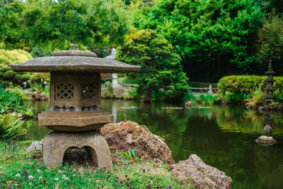 Tranquil view of a Japanese garden featuring a stone lantern by a pond surrounded by lush greenery.