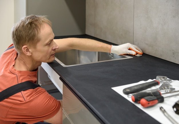 The plumber is setting the start button for the waste shredder on the kitchen sink.