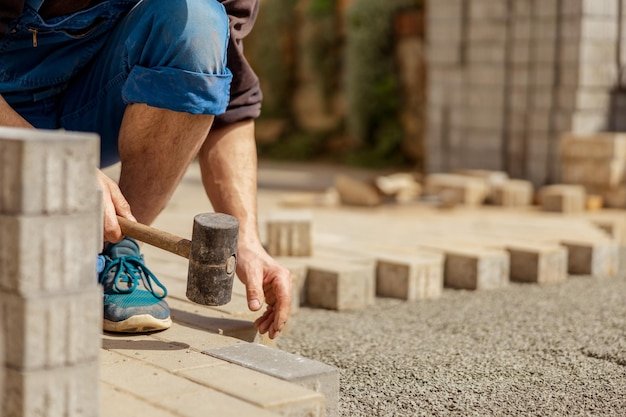 Young man laying gray concrete paving slabs in house courtyard on gravel foundation base Master lays paving stones Garden brick pathway paving by professional paver worker Repairing sidewalk