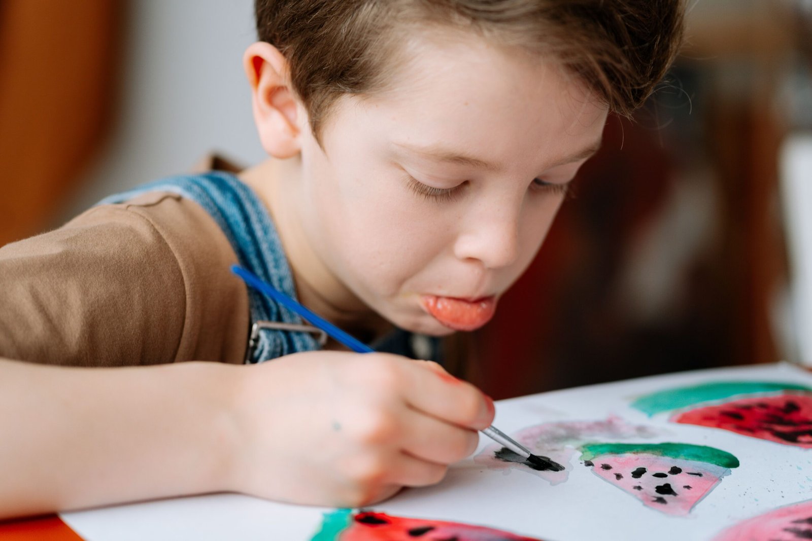 A focused child painting a watermelon with a brush in an art class setting.