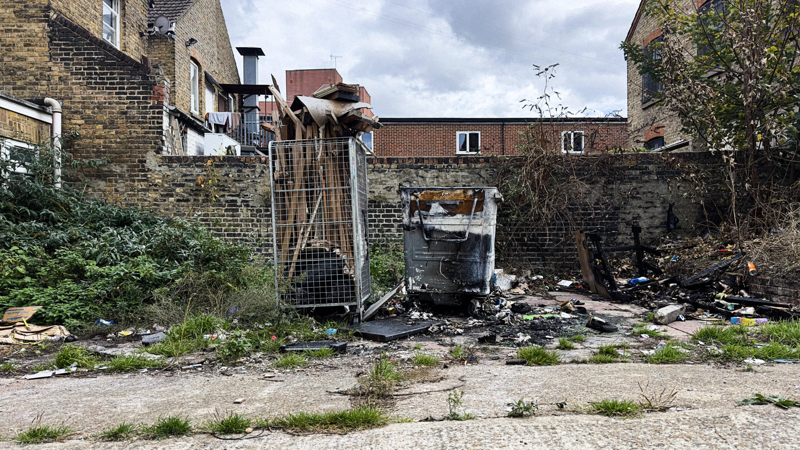 Wide view of burnt wheelie bins, construction debris, and litter in the fly-tipped area behind 330 High Street in Chatham, Kent