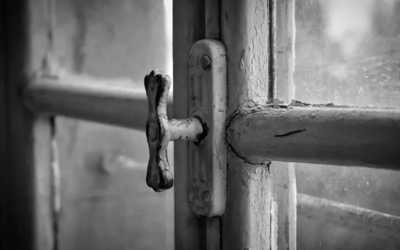 Close-up of an old, rustic window handle in black and white.