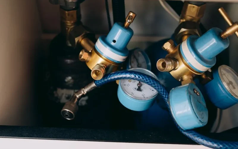 Detailed view of blue and brass gas pressure regulators with gauges and tubing in an industrial setting.