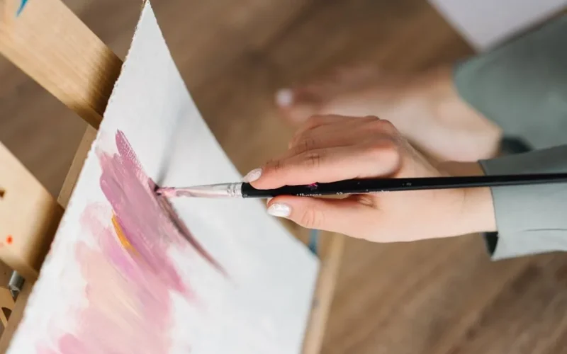 Artist's hand painting with brush on canvas, capturing creativity and artistry.