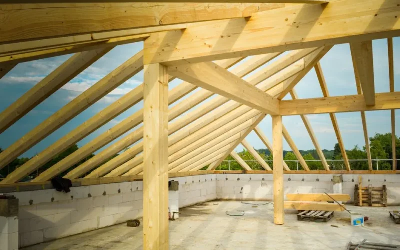 Unfinished construction site with a focus on wooden roof trusses under a clear sky.