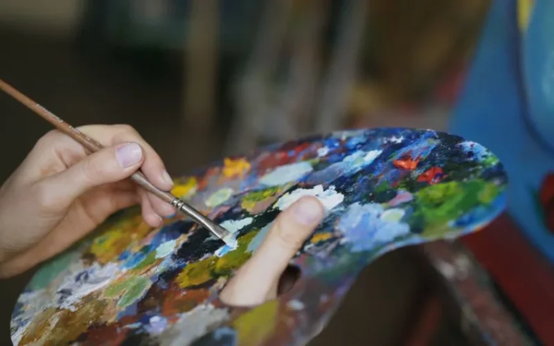 Close-up of an artist's hand mixing vivid colors on a palette using a brush.