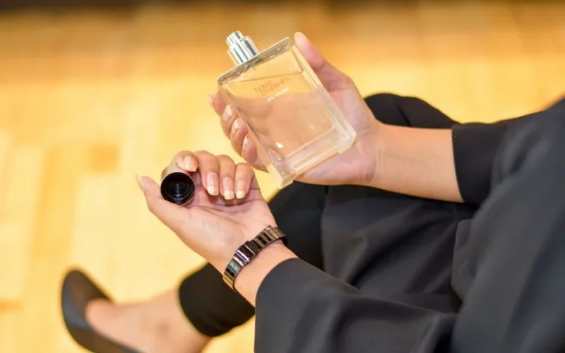 Close-up of a woman holding a Terre d'Hermes perfume bottle indoors, showcasing elegance and luxury.