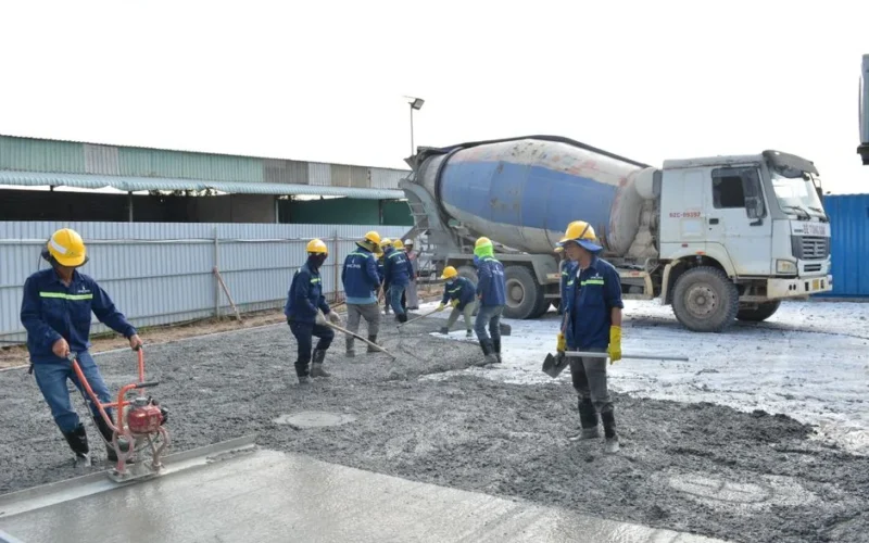 Workers in safety gear pouring concrete outdoors with a cement mixer truck.