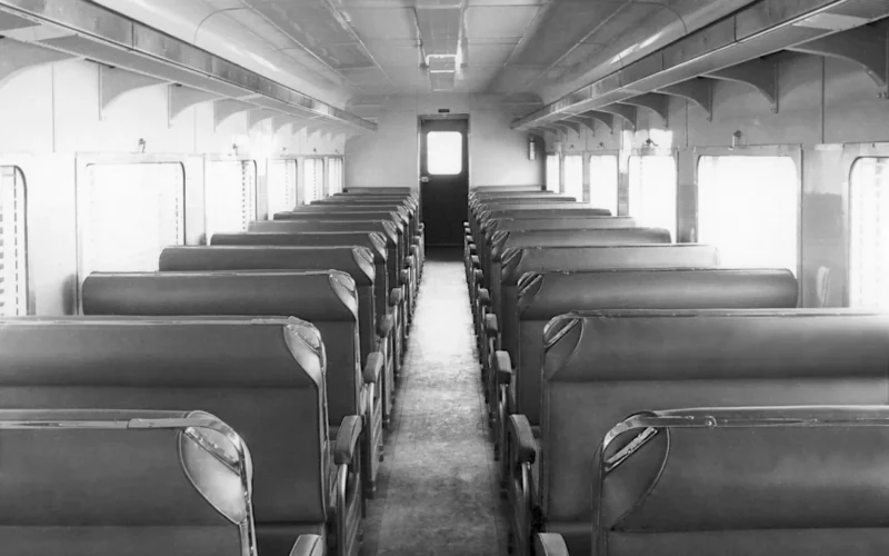 Interior of a "Bluebird" railcar (250 class second-class passenger power car) which the South Australian Railways introduced in the 1950s. The direction of seats in this 250 class power car was easily changed by pulling or pushing the grips shown so that passengers could choose the direction and combination they preferred for their long country journeys. In the 100 class non-power cars, second-class seating was the same; the first-class seats rotated and reclined. The winding handles above each double-glazed window allowed venetian blinds between the panes to be lowered, raised and angled. Diffused lighting and air conditioning were innovative at the time.
