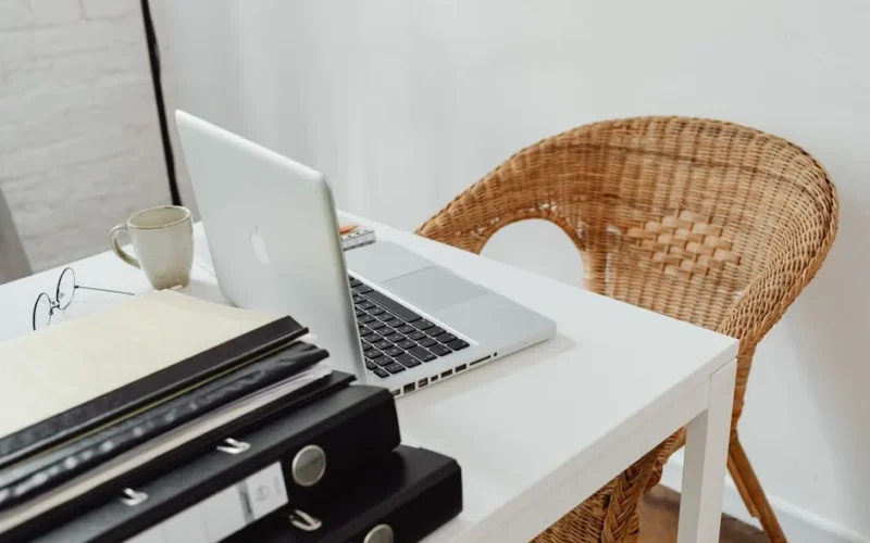 A cozy home office setup featuring a laptop, binders, and wicker chair for productive remote work.