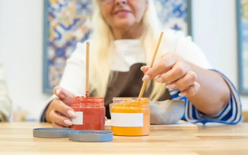 Close-up of a senior woman mixing red and orange paints in a Portuguese art studio.
