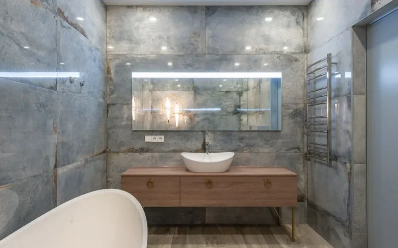 Creative design of bathroom with washstand on cabinet under mirror on stone wall against bathtub in house