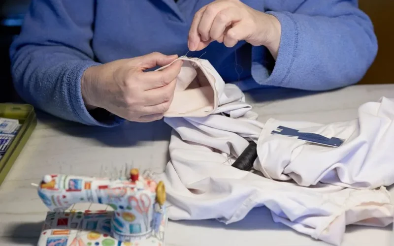 A person sewing a garment by hand, focusing on the intricate stitching work.