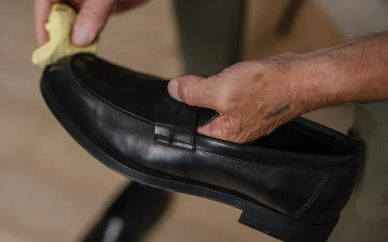 Detailed shot of hands polishing a black leather shoe with a cloth indoors.