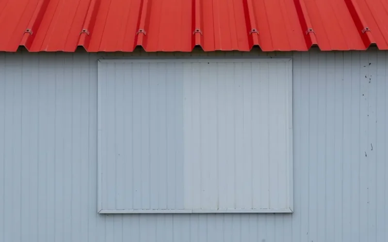 Minimalist image of a red metal roof with blue-grey corrugated panel wall.