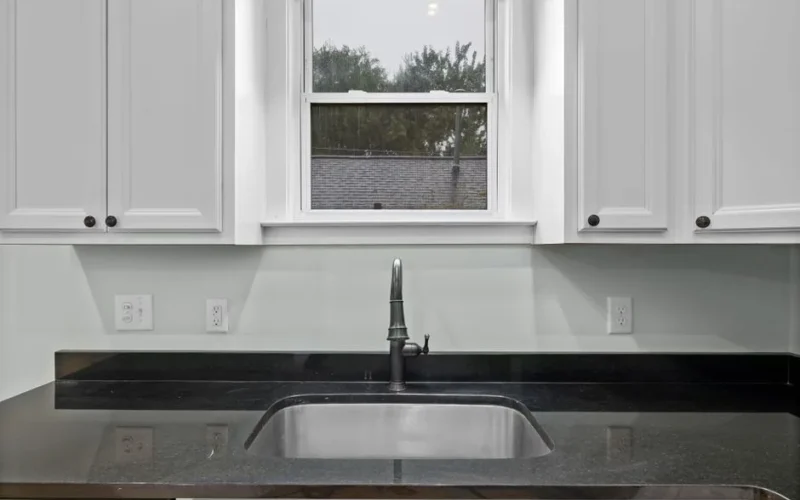 Elegant kitchen interior highlighting a sleek sink, black countertop, and white cabinets under natural light.