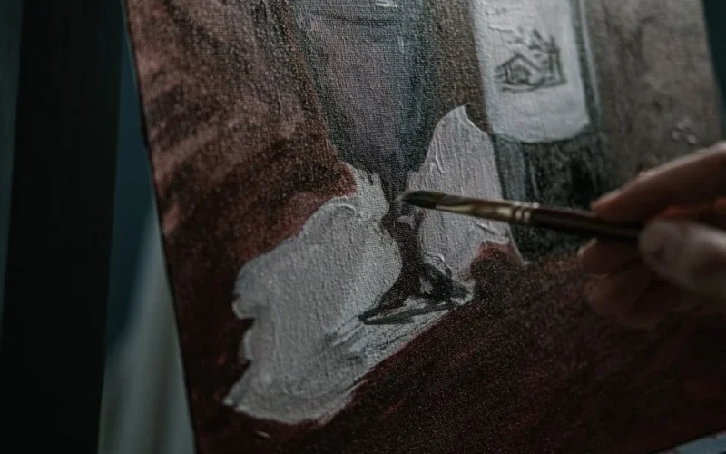 Artist hand painting on canvas with brush, detailed artwork creation in process.