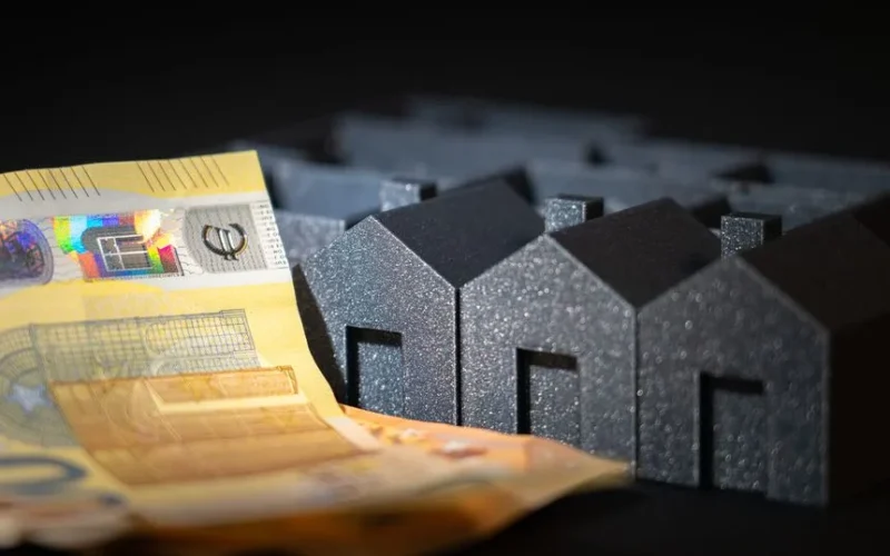 Close-up of black miniature houses with Euro notes, representing real estate investment and savings.