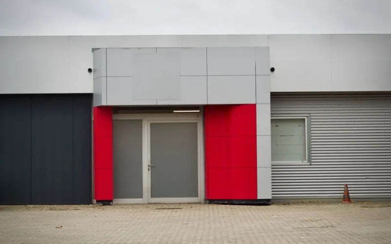 Front view of a modern industrial building entrance with red accents and metal cladding.