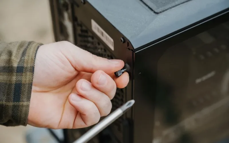 Close-up of a hand unscrewing a desktop computer case, emphasizing technology maintenance.