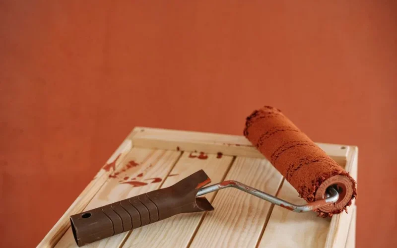A paint roller with rustic brown paint on a wooden surface against an earthy wall.