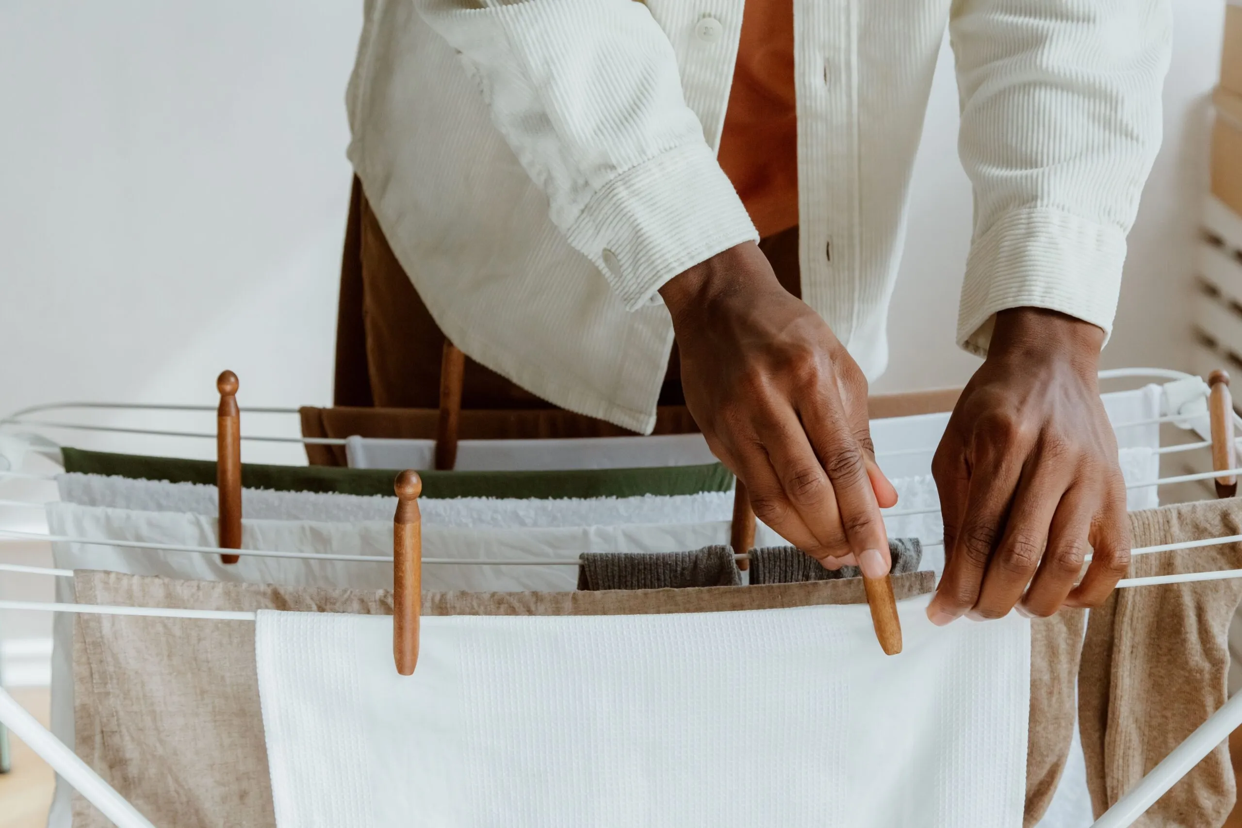 Close-up of a man hanging fresh laundry on a drying rack indoors, emphasizing cleanliness and domestic life.