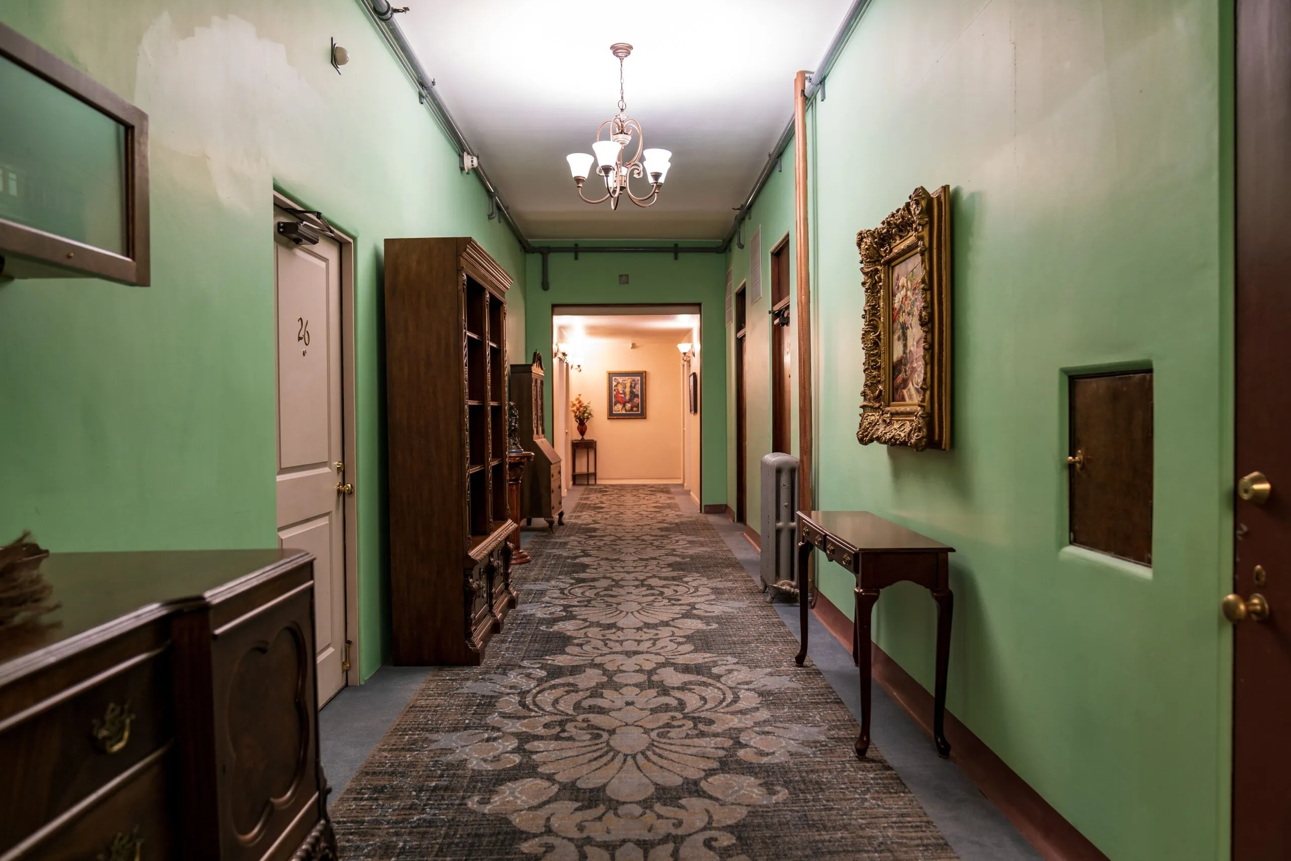 A vintage-style hotel hallway adorned with classic furnishings and a chandelier.