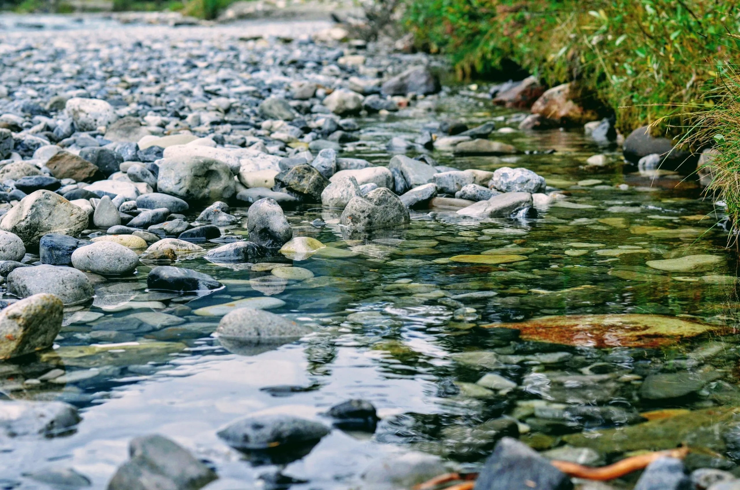 Peaceful rocky creek with clear water reflecting natural surroundings in a tranquil outdoor setting.