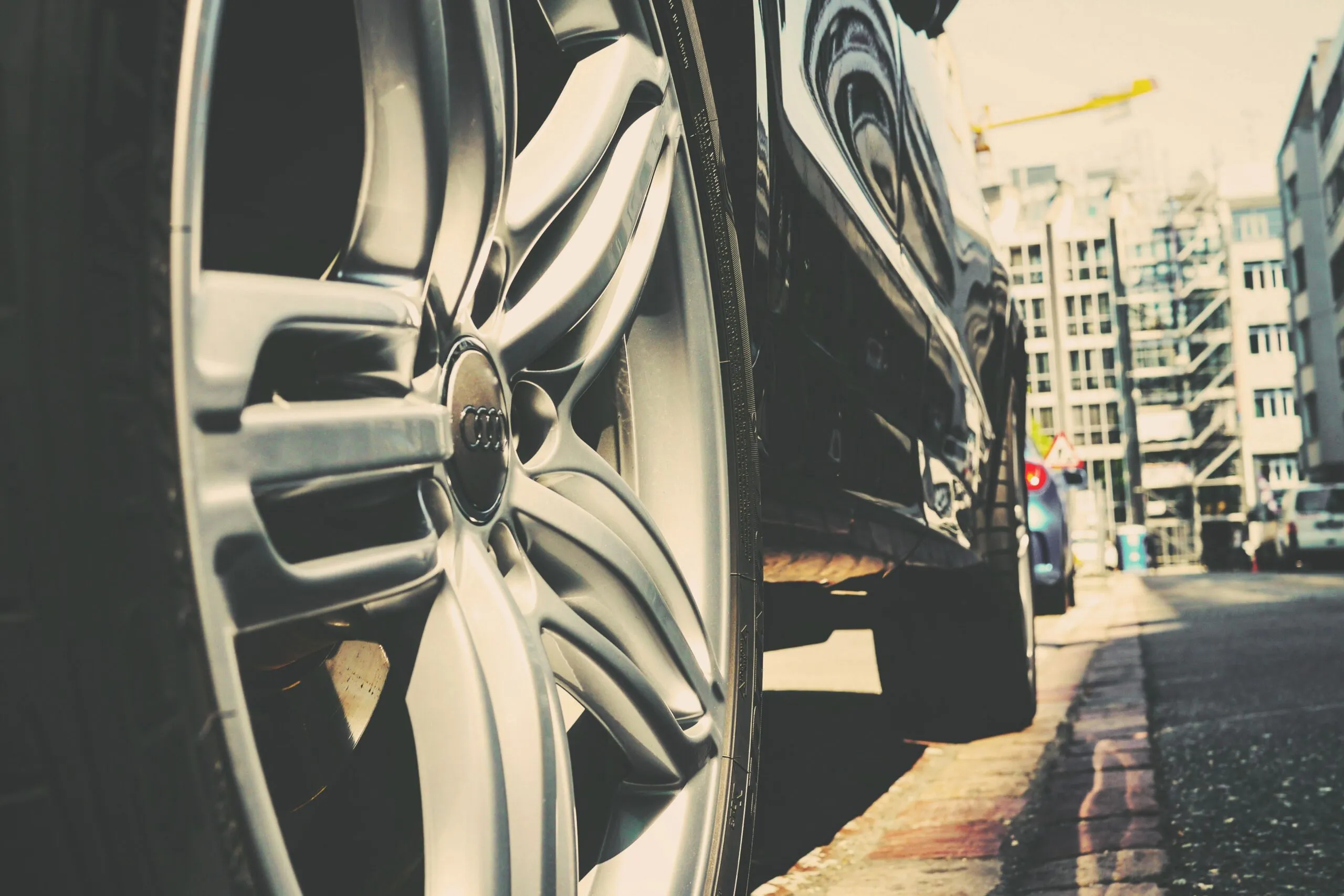Detail of a car wheel on a city street with buildings in the background. Urban vibe.