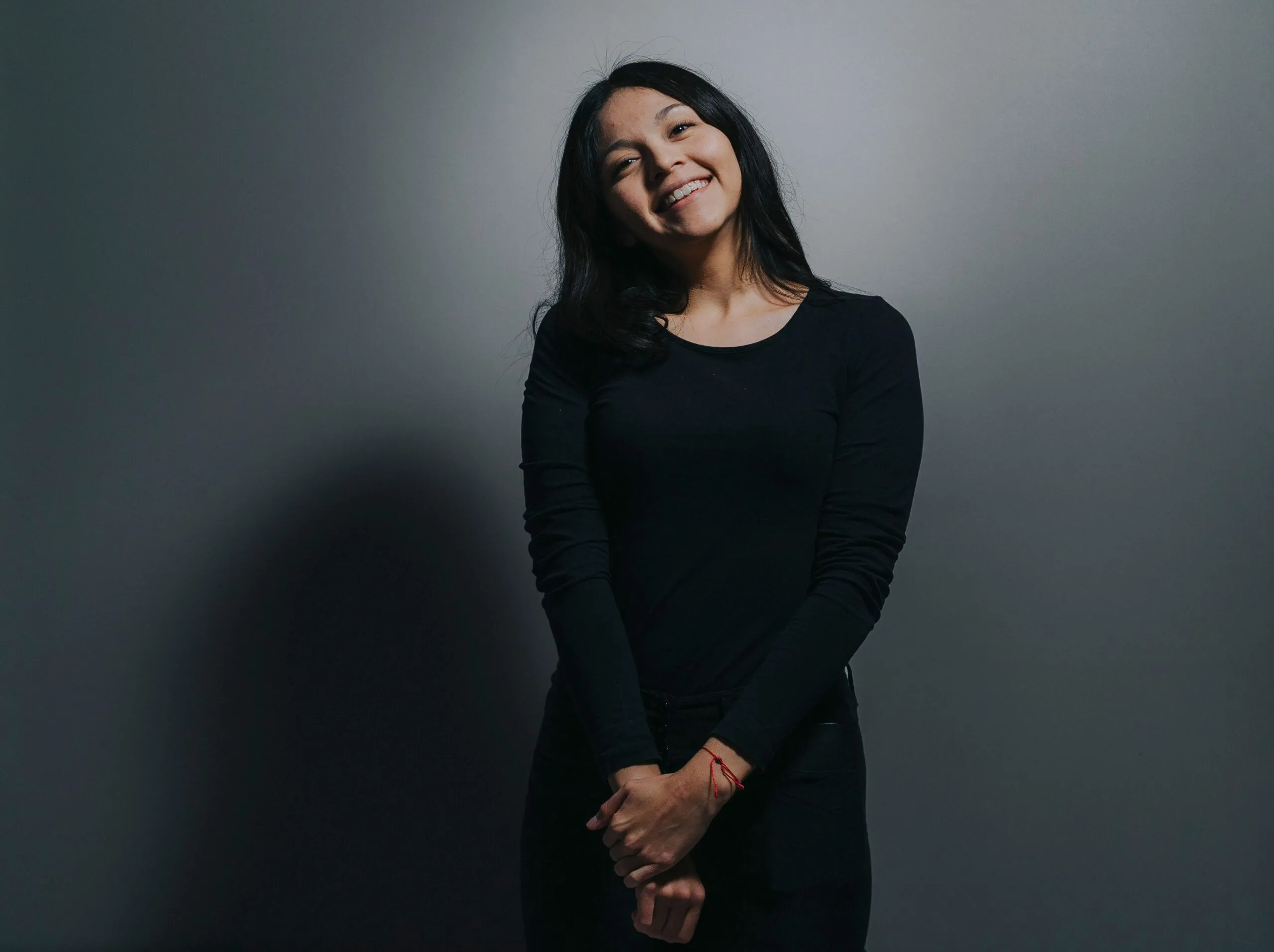 Simple portrait of a woman in black clothing smiling against a gray background.