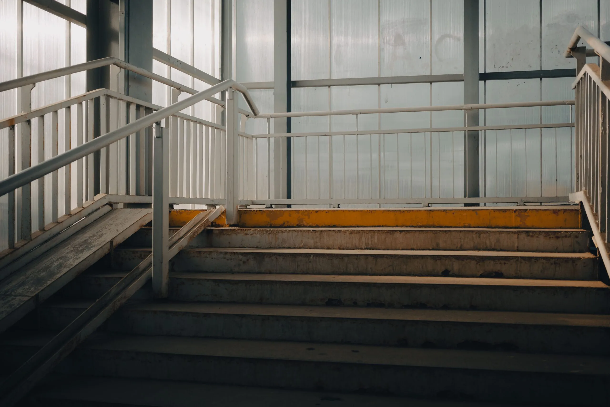 Empty industrial-style staircase indoors with metal railings and natural lighting.