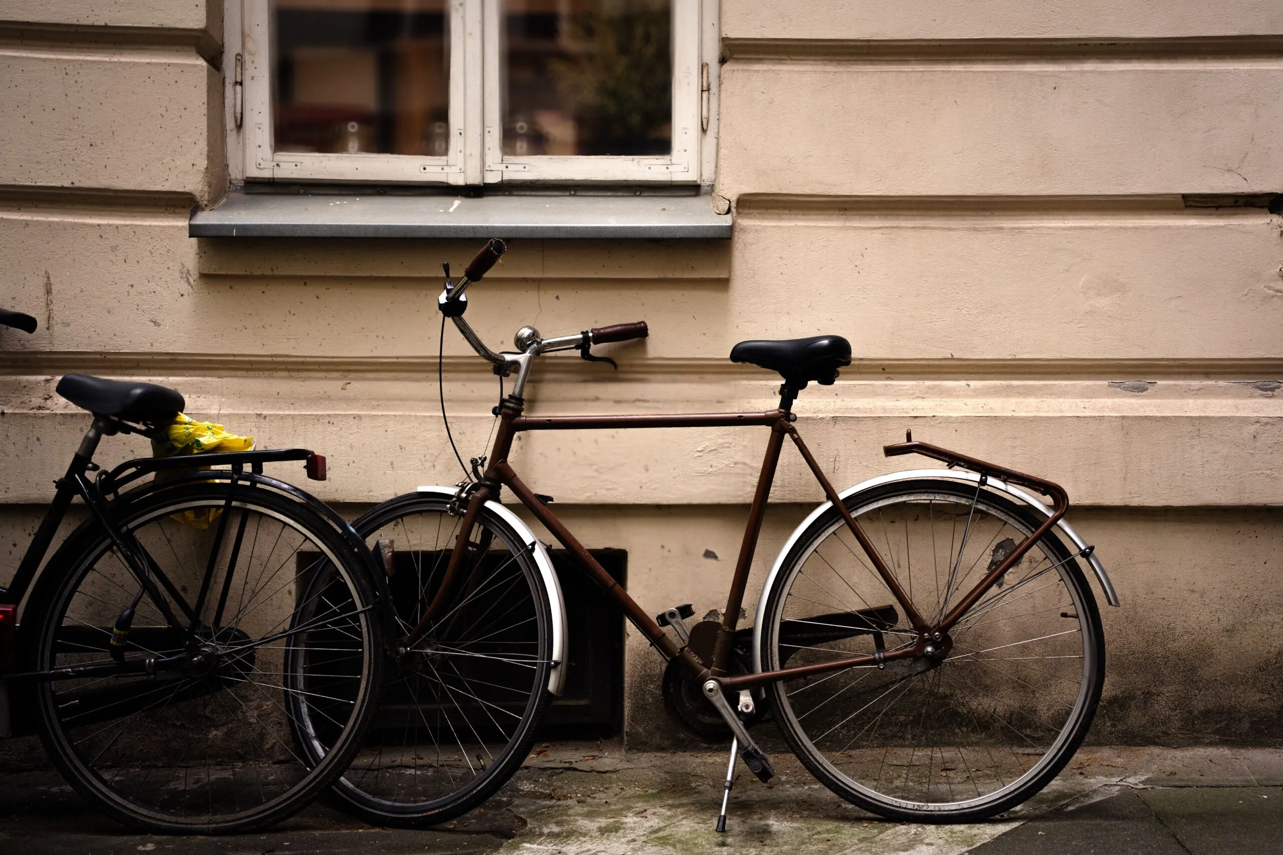 Two vintage bicycles parked against a rustic beige wall, creating a nostalgic urban scene.