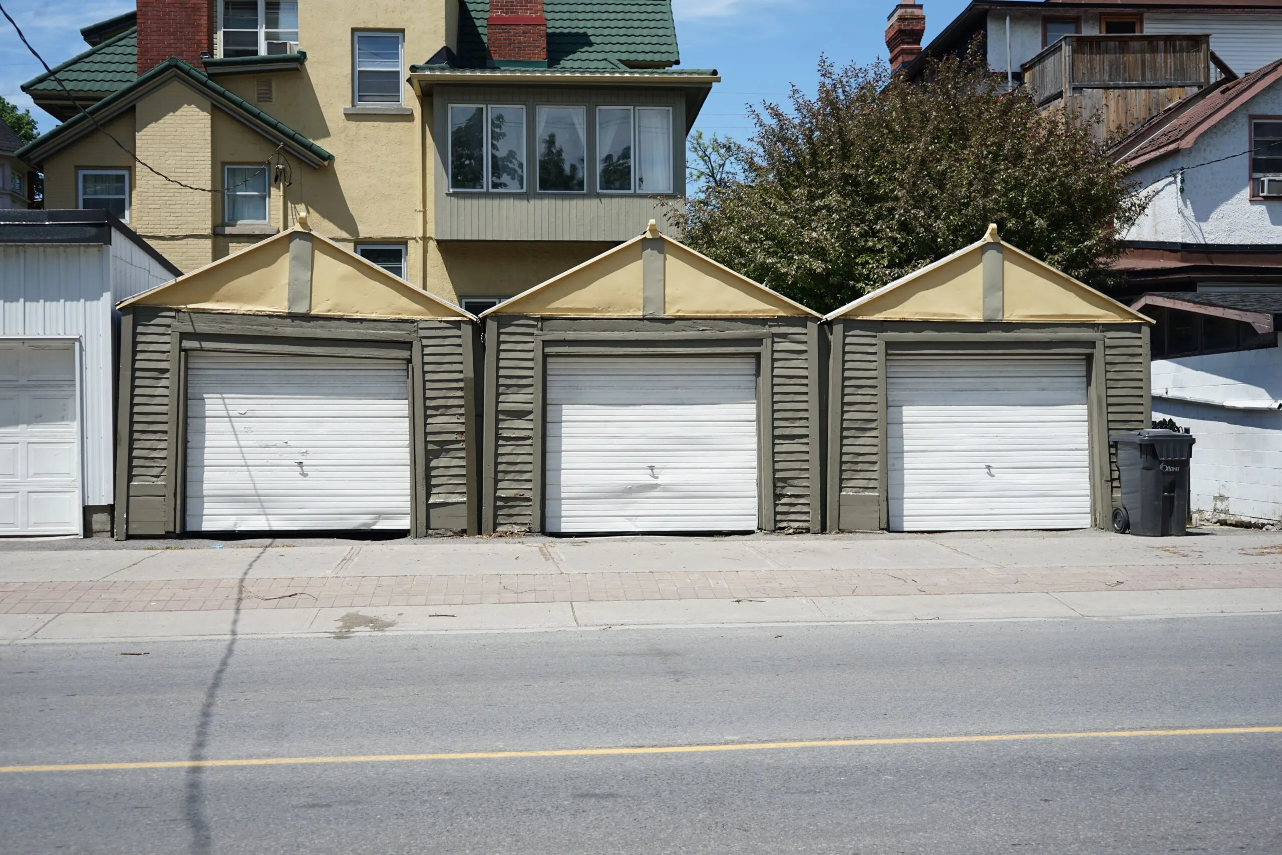 Row of three traditional residential garages with unique roof design on a sunny day.
