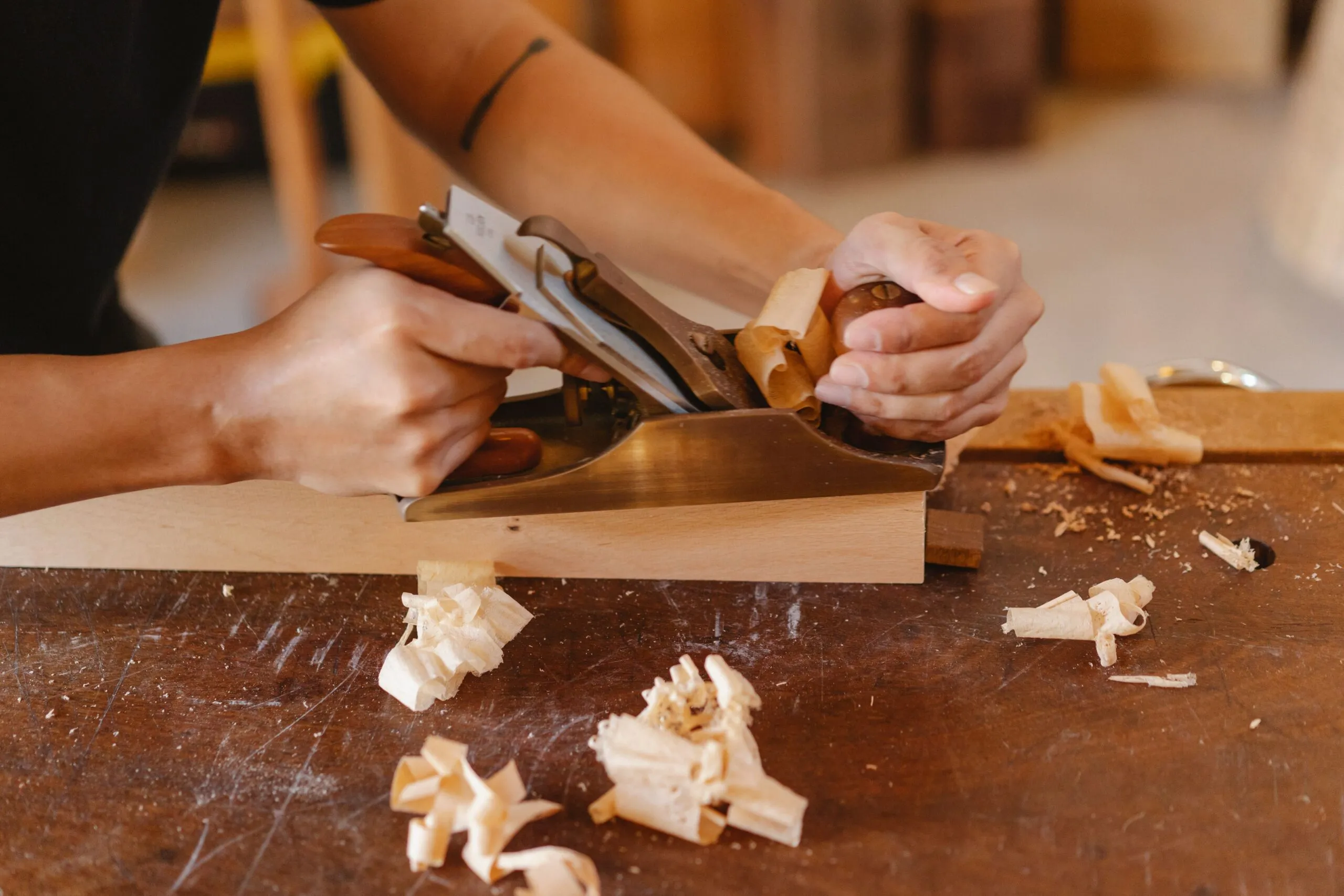 From above of crop anonymous male working with timber plank and jack planer on table in workshop