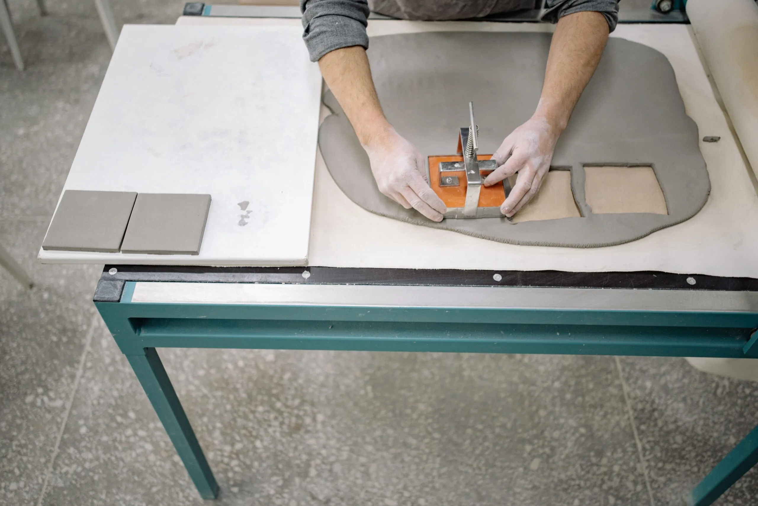 A person shaping clay using a cutter to craft tiles on a worktable.