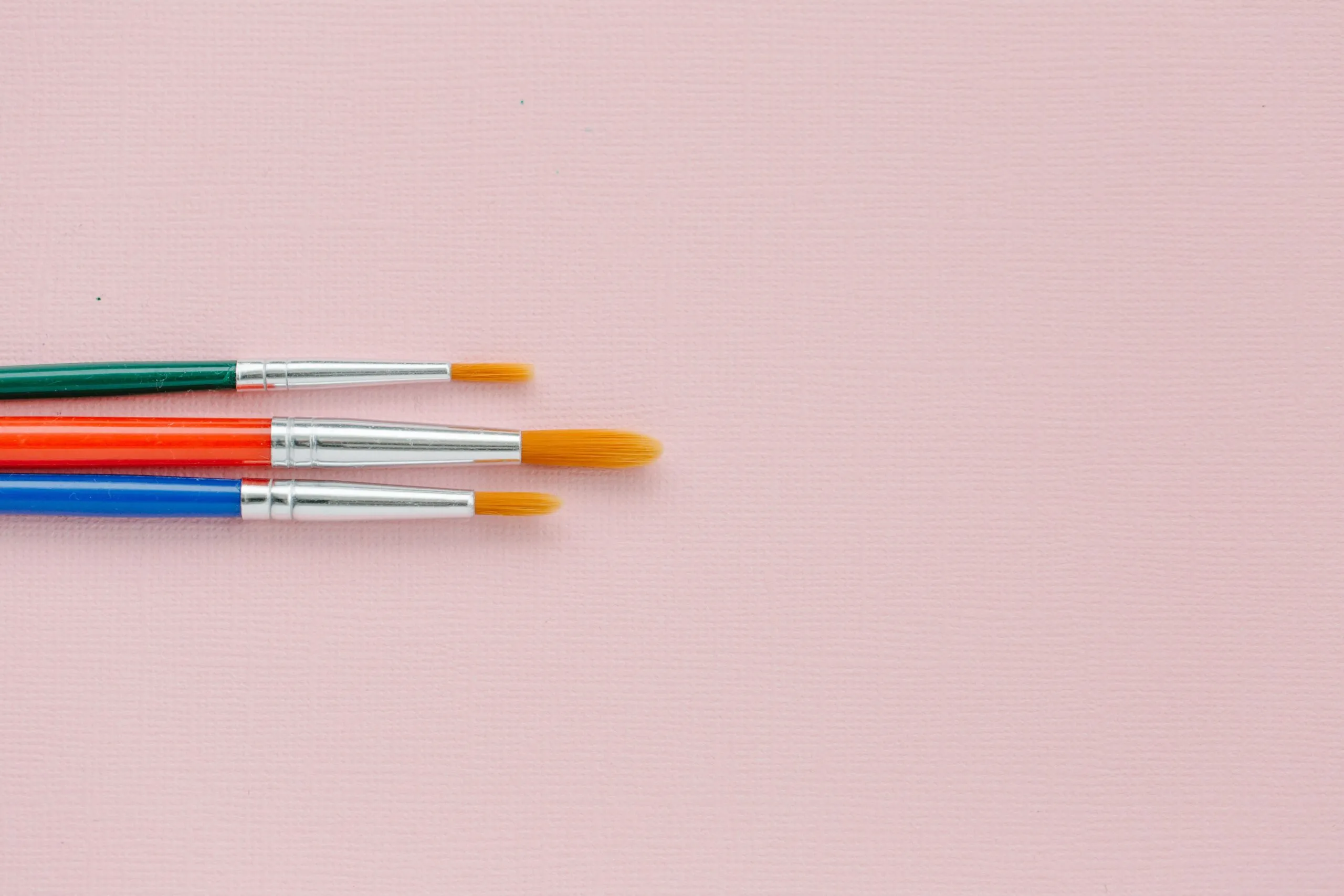 Three vibrant paintbrushes on a pink canvas providing ample copy space.