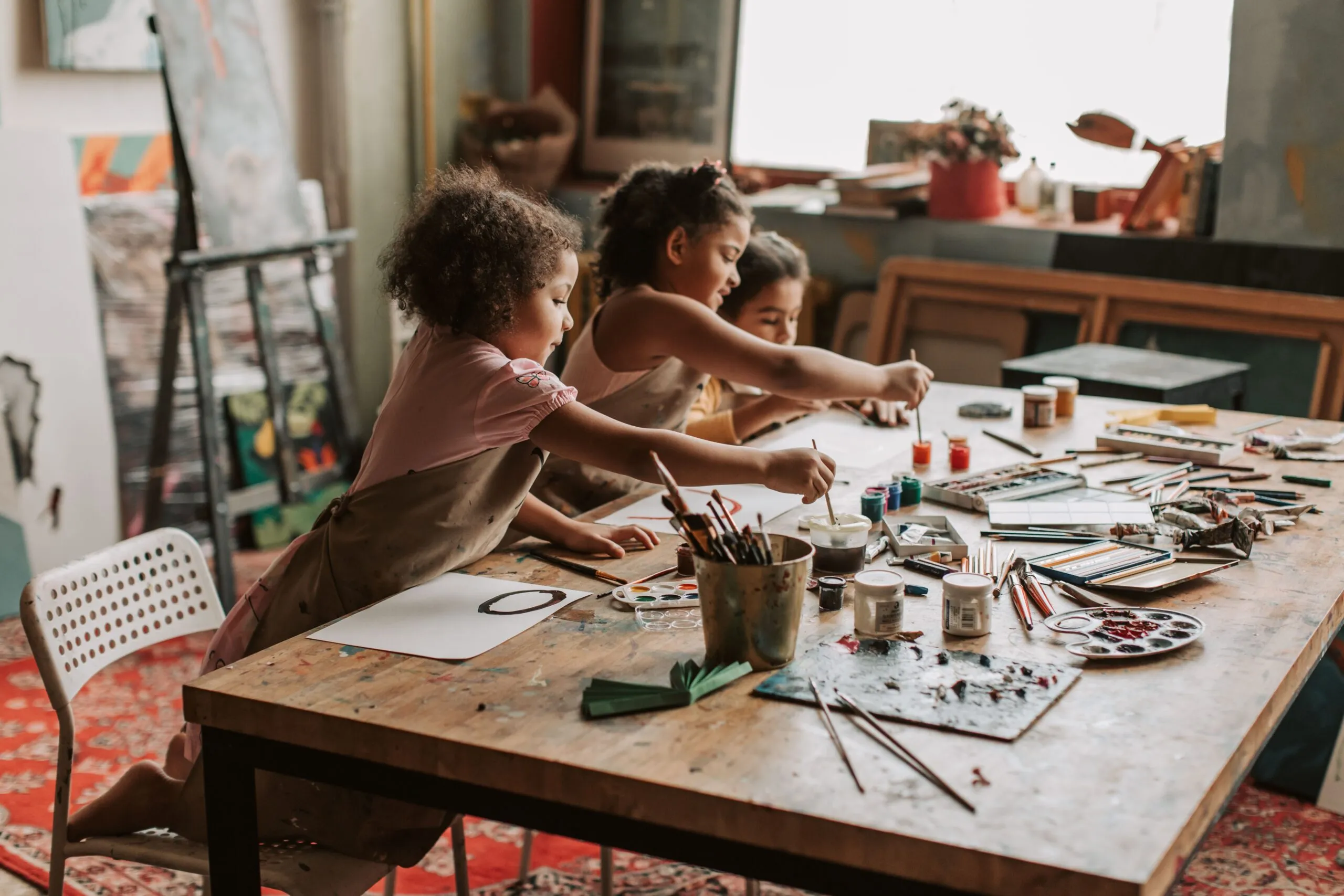 Three young girls engaged in painting at an indoor art studio, exploring their creativity.